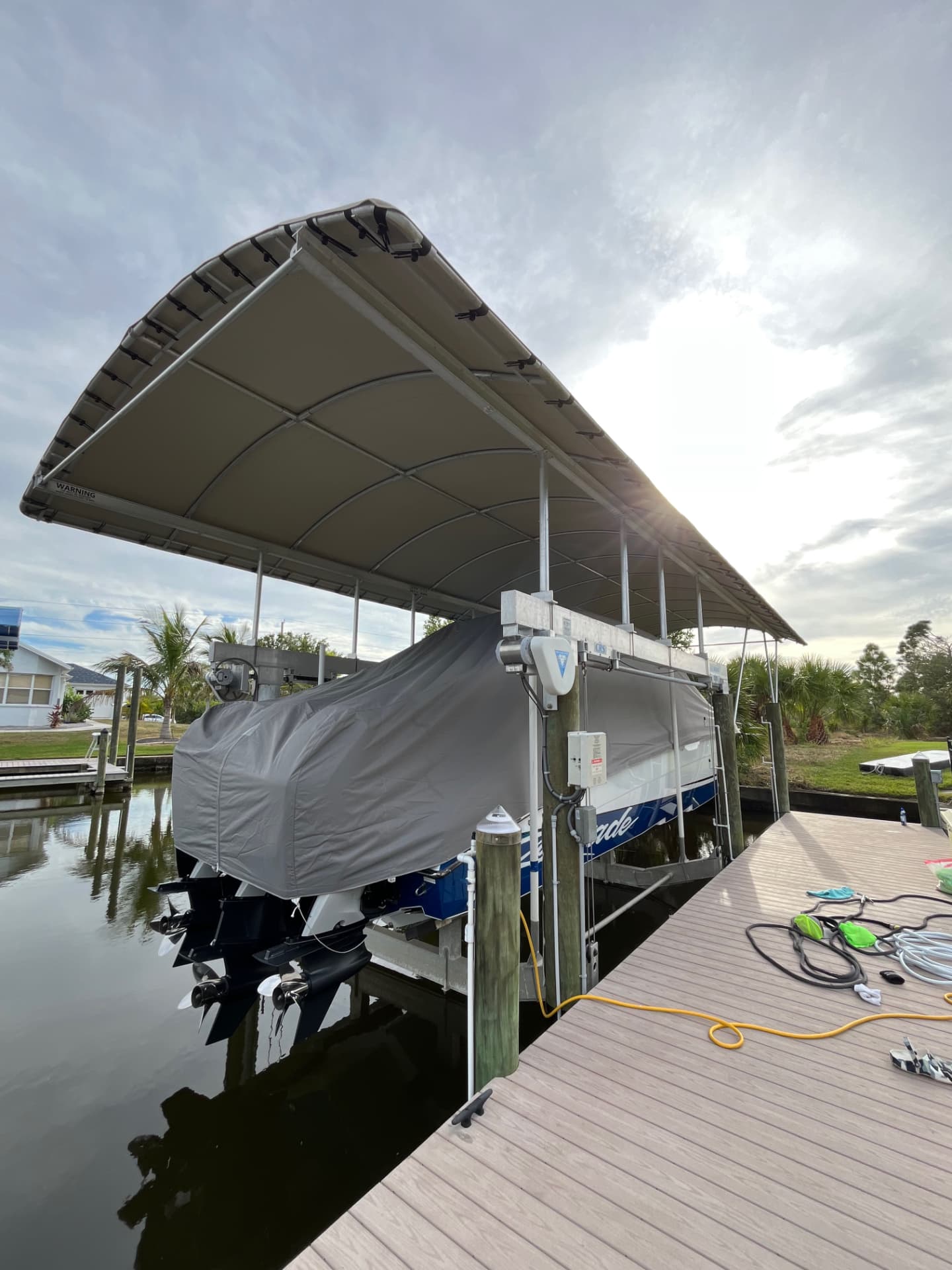 Covered vessel on a canopied lift at a private dock, shore cord and gear laid out on the decking